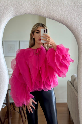 A woman wearing a hot pink long sleeve tulle ruffle blouse with a mock neck and tie back closure.
