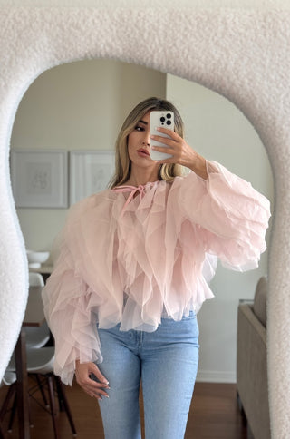 Person wearing a pink ruffled blouse and blue jeans taking a mirror selfie.